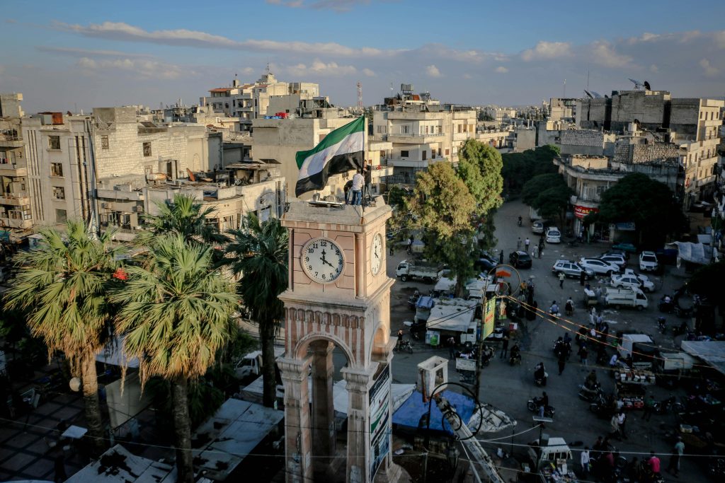 Aerial view of a vibrant city square with a clock tower and palm trees in Idlib, Syria.
