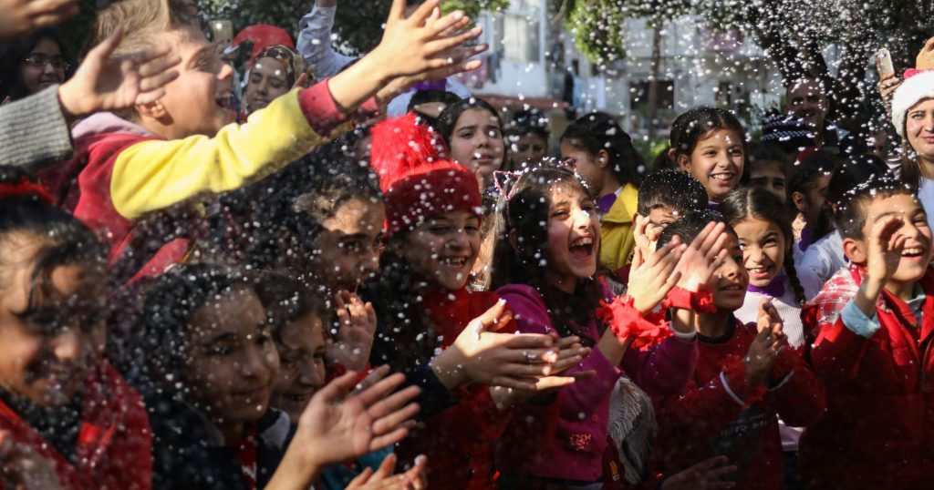 Children joyfully celebrate under falling snow in a vibrant Syrian street scene.
